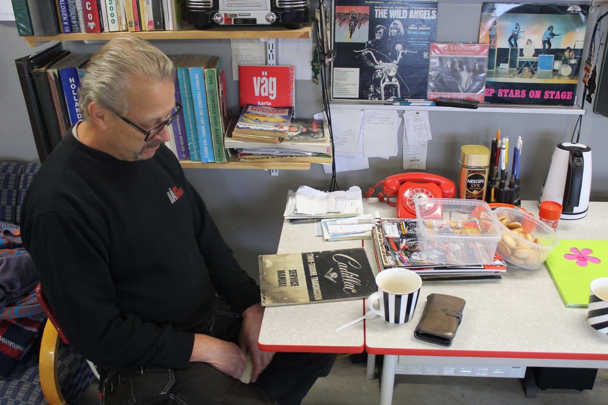 Börje i kaffehörnan med Perstorps bord och rätt litteratur och musik Cadillac Service manual och HEP STARS ON STAGE i hyllan
