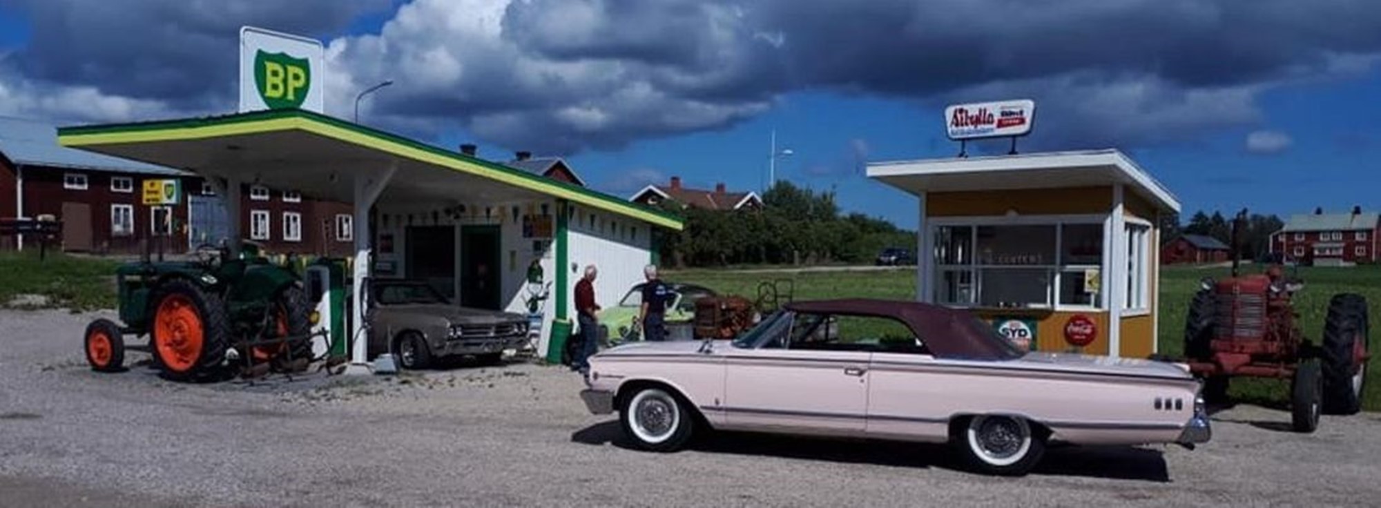 Kan det bli mer svenskt från en svunnen tid än detta? En Mack o Sibylla kiosk, lite amerikanska bilar och några bönder som svängt in på macken med sina traktorer och står och diskuterarar kring en Saab trubbnos.